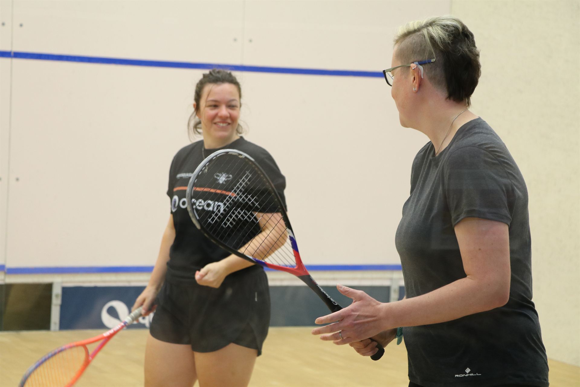 A female squash coach laughing with a beginner during a session at a Manchester squash court
