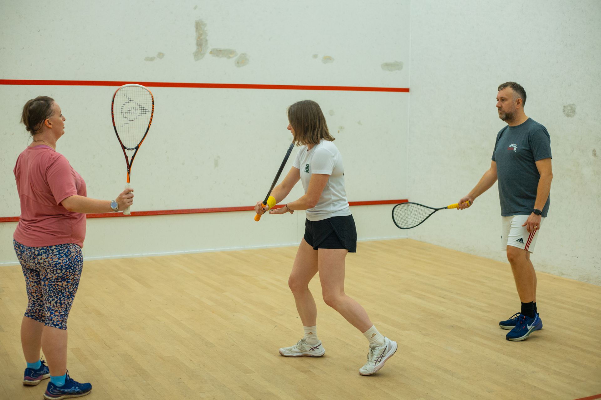 A squash coach and a couple practising their swing on court