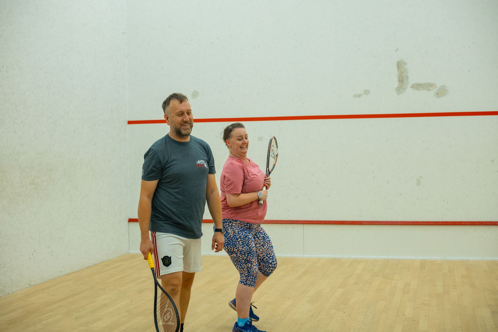 A couple laughing as they walk across a squash court together