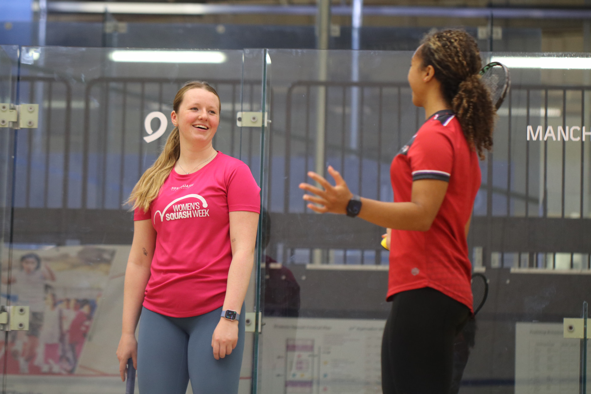 Two squash players smiling and chatting between games on a glass-back court