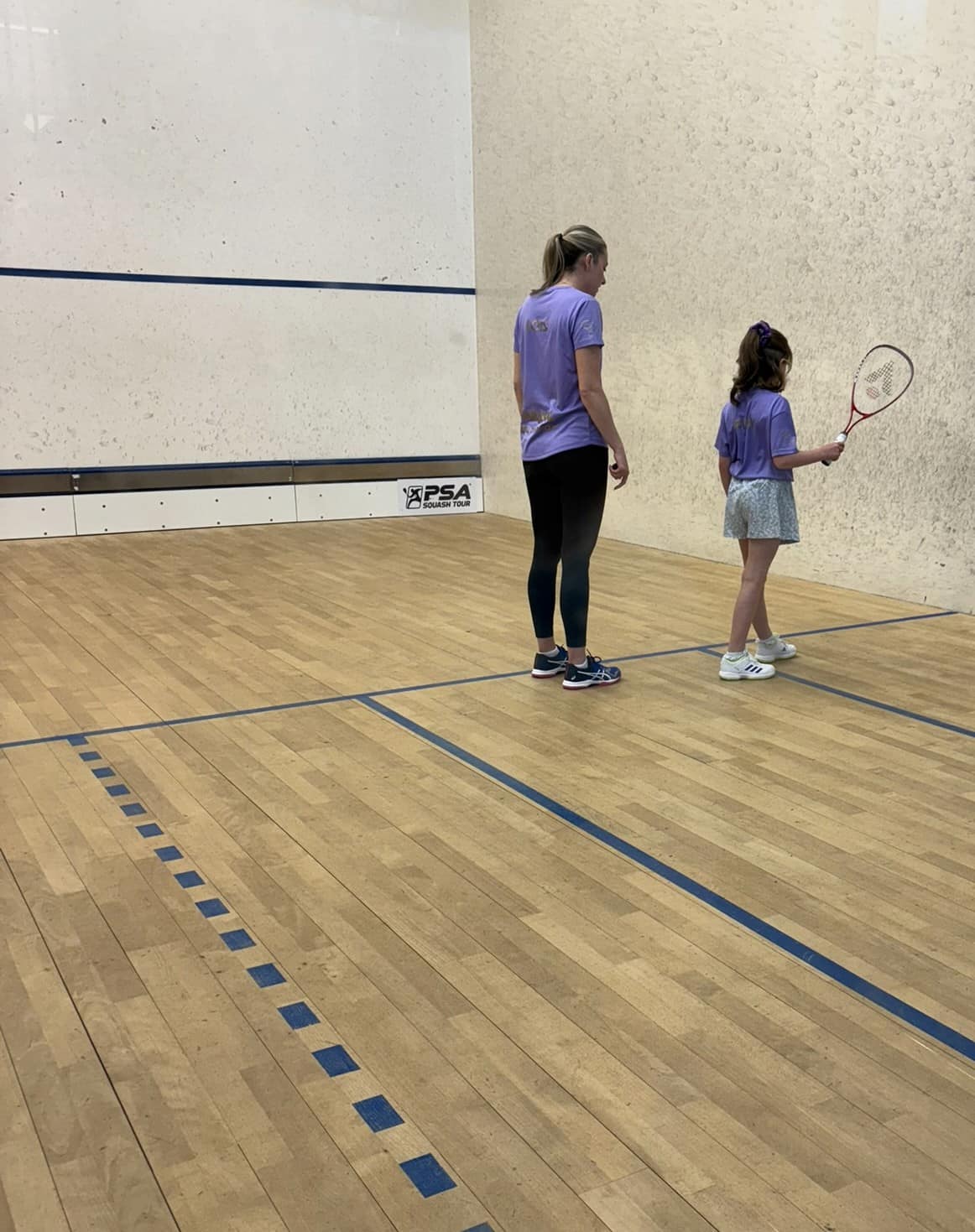A female squash coach giving a junior coaching session to a young child aged 5-17 on a UK squash court