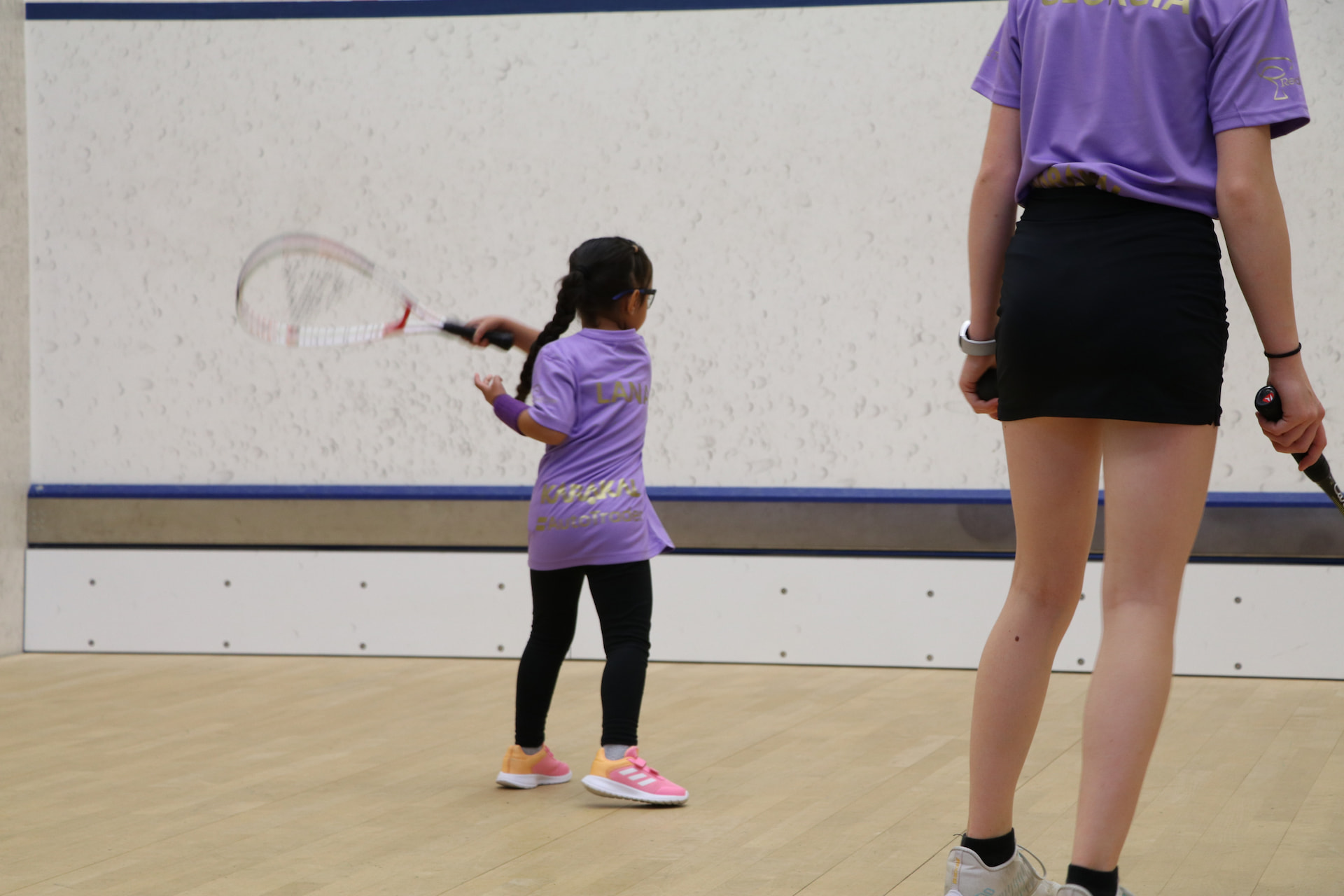 Young girl practising her swing with a coach watching during a junior squash session
