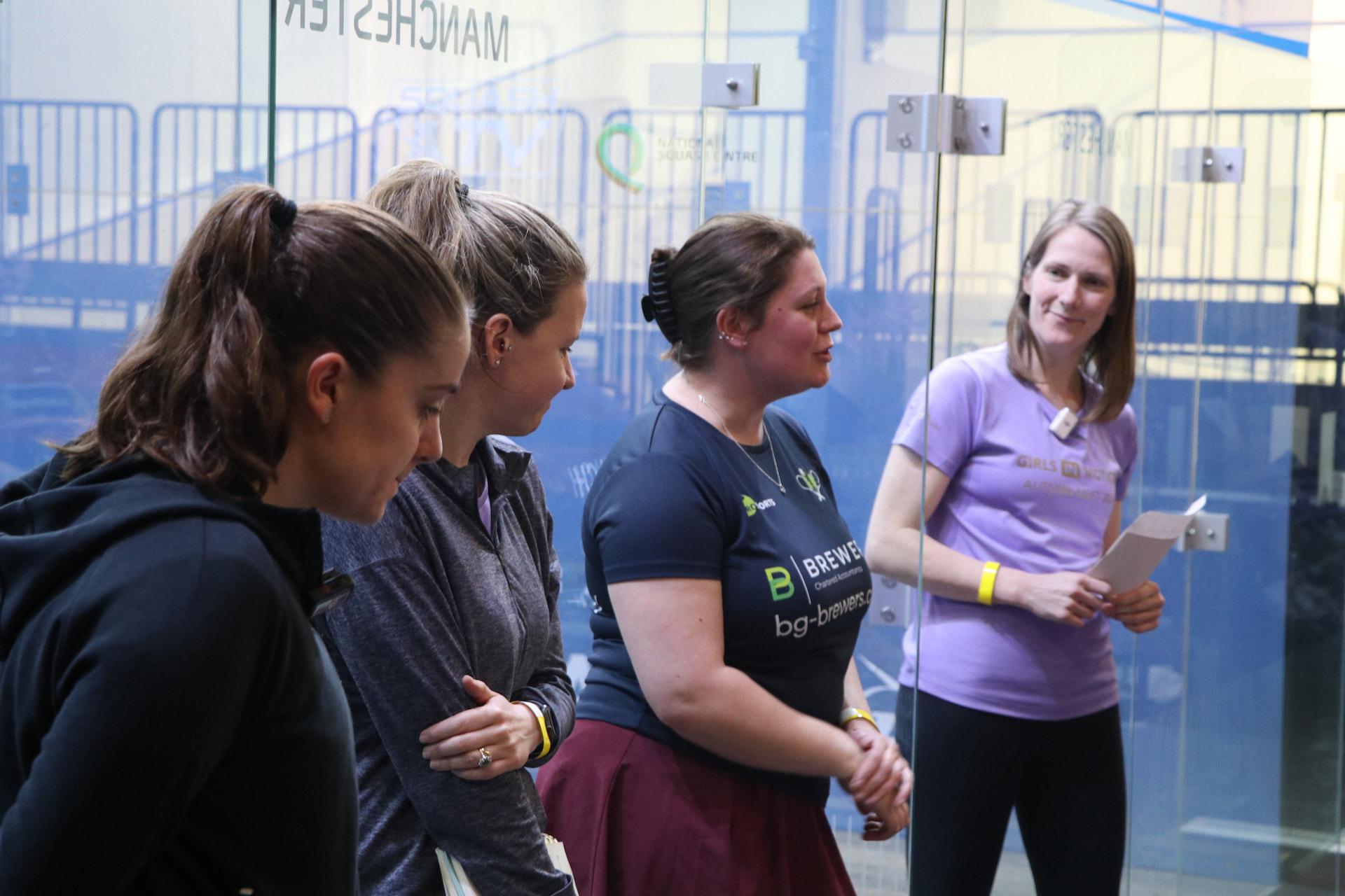 Female squash coaches gathered on a glass-back court at the National Squash Centre in Manchester
