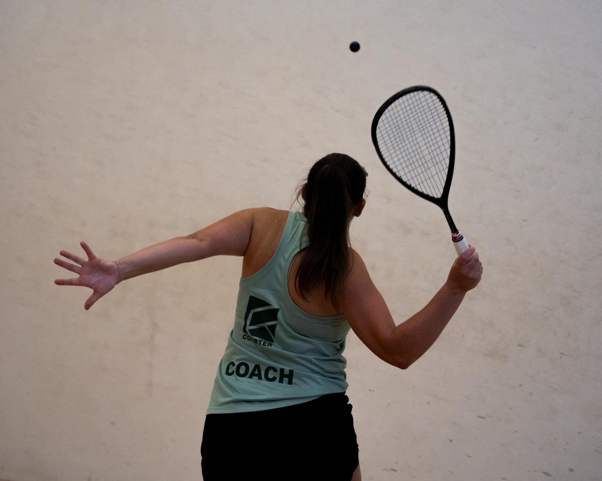 A coach seen from behind with her racket raised and the ball in the air above her
