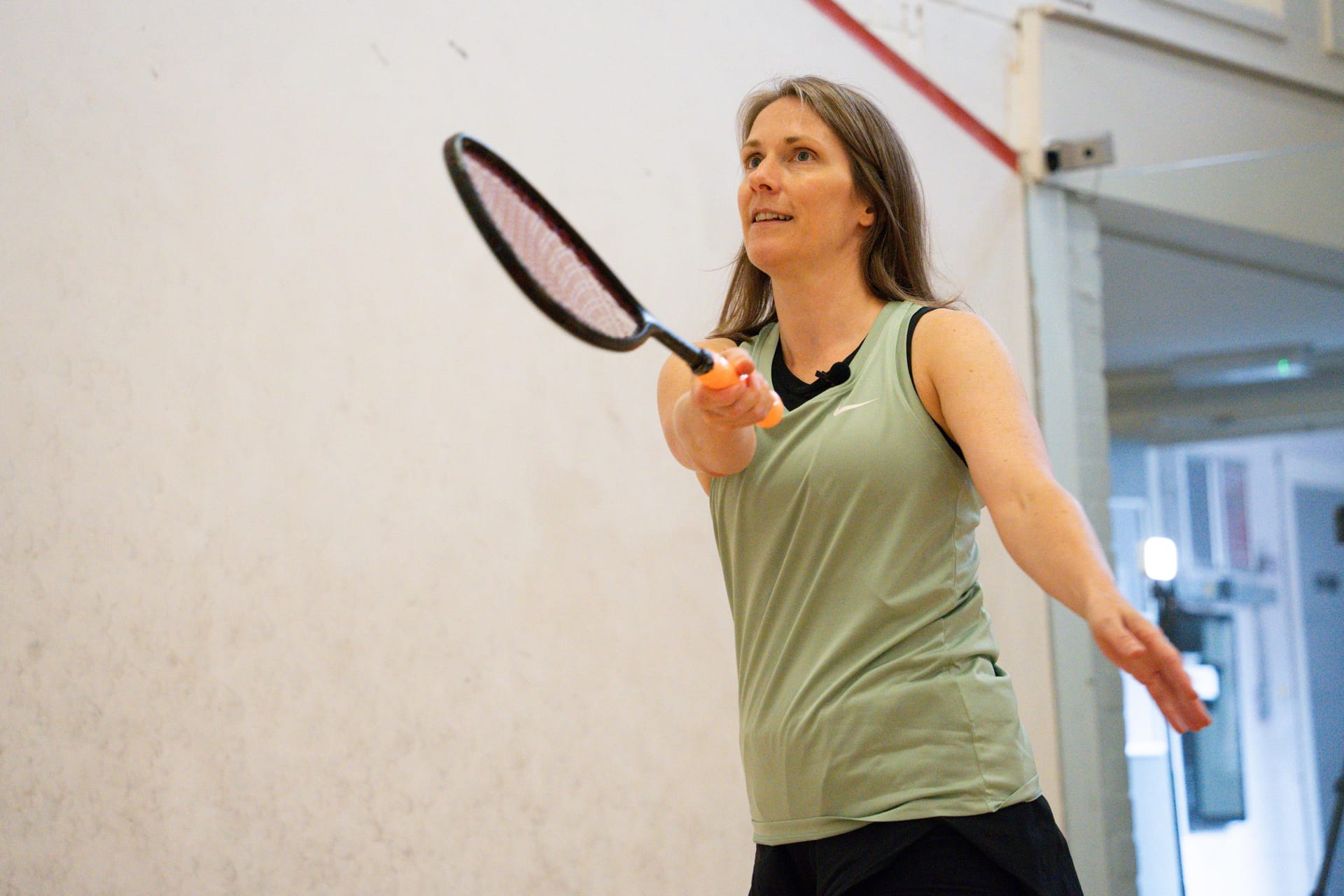 A coach in a mint Courter vest volleying on a squash court