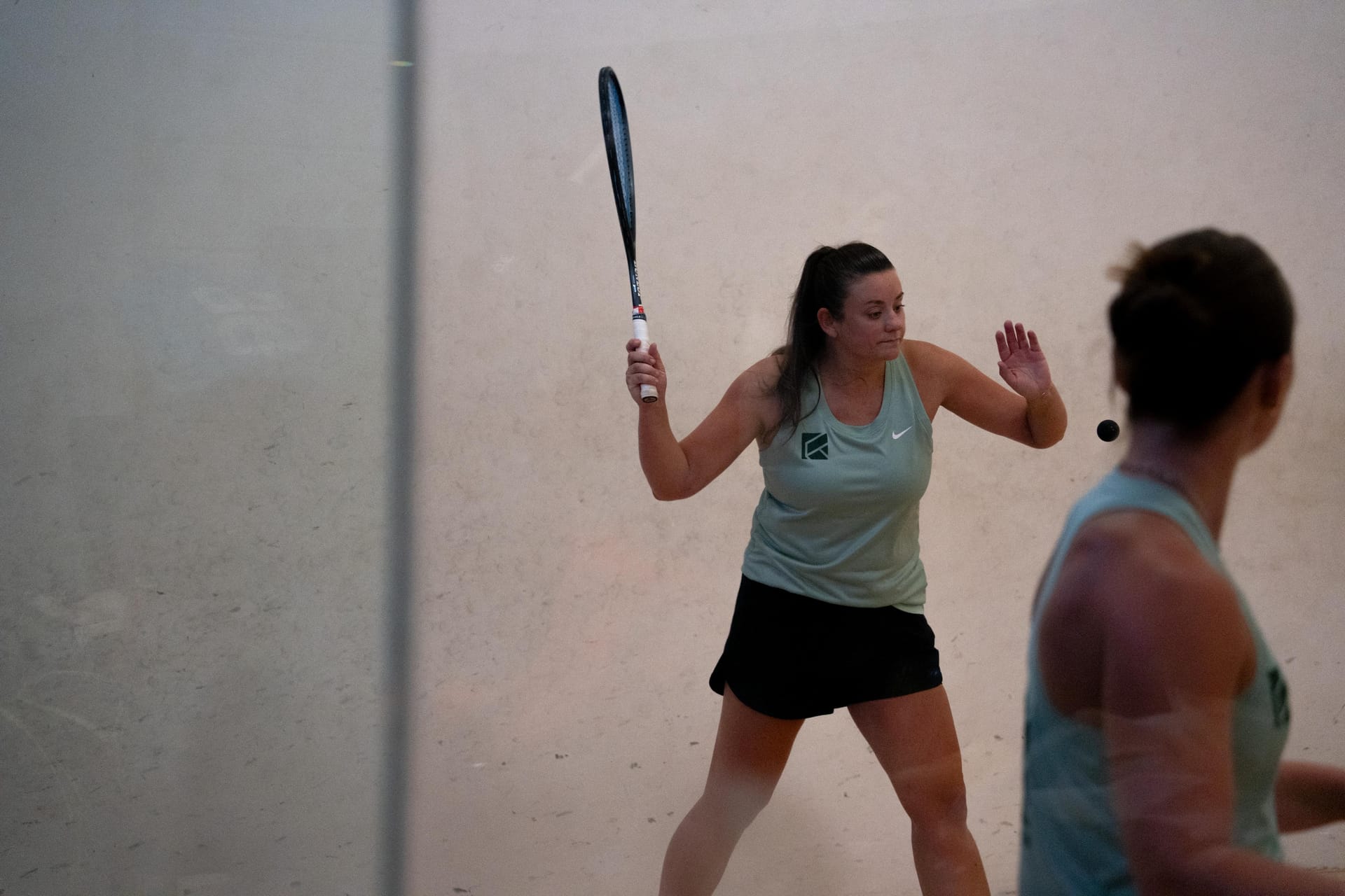 Two players in mint Courter vests on court, one about to strike the ball