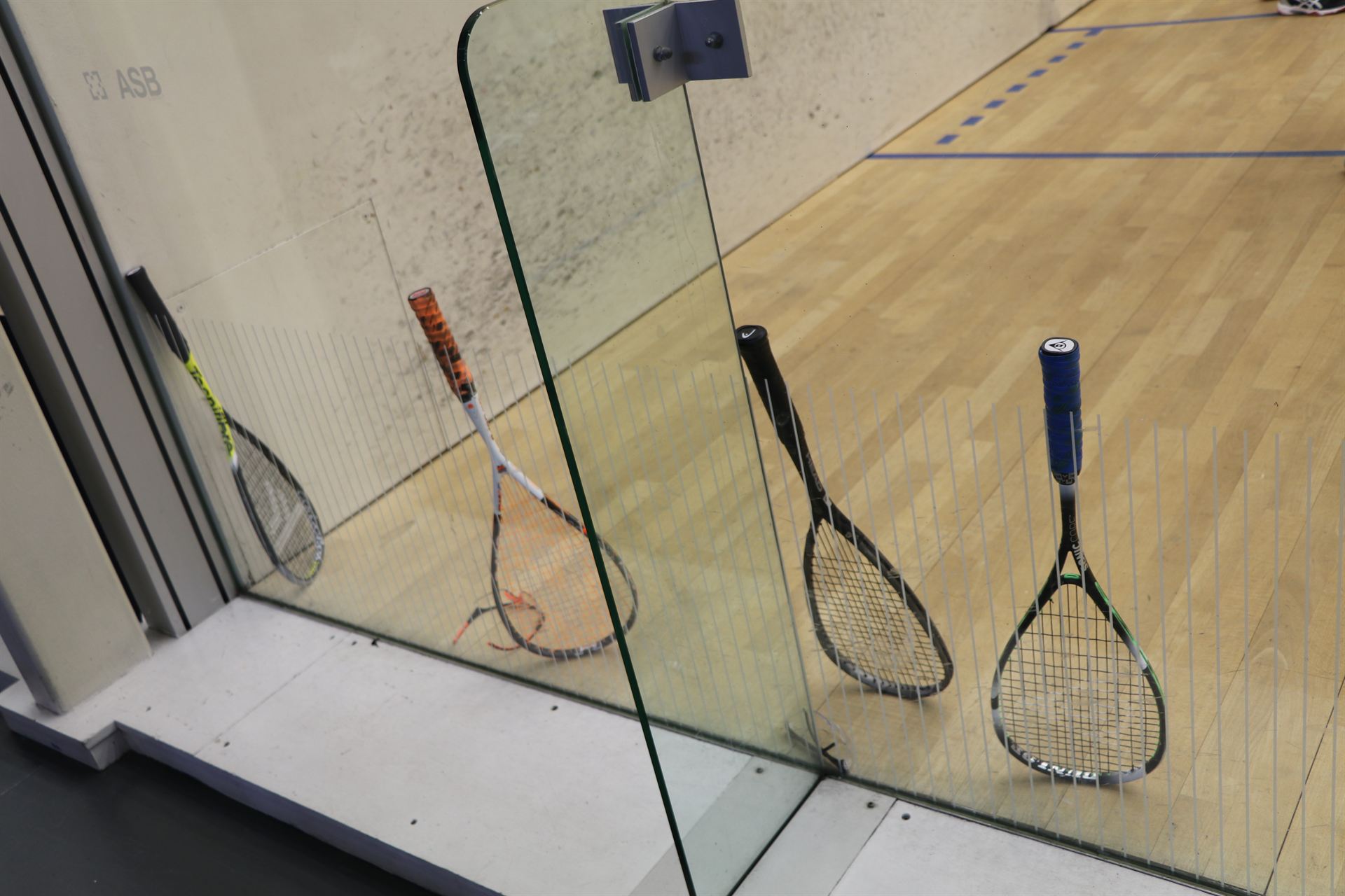 Two squash rackets resting against a court wall before a group coaching session