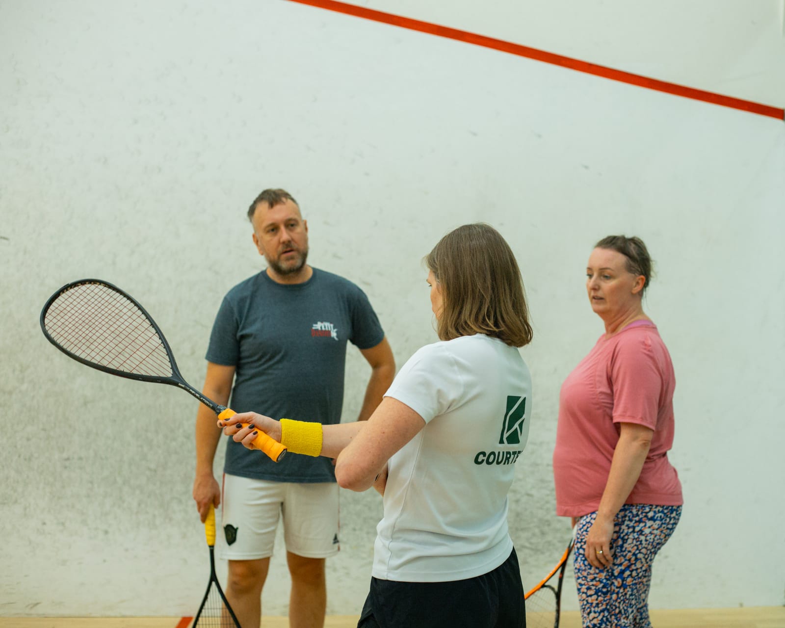 A coach showing a couple how to hold a squash racket