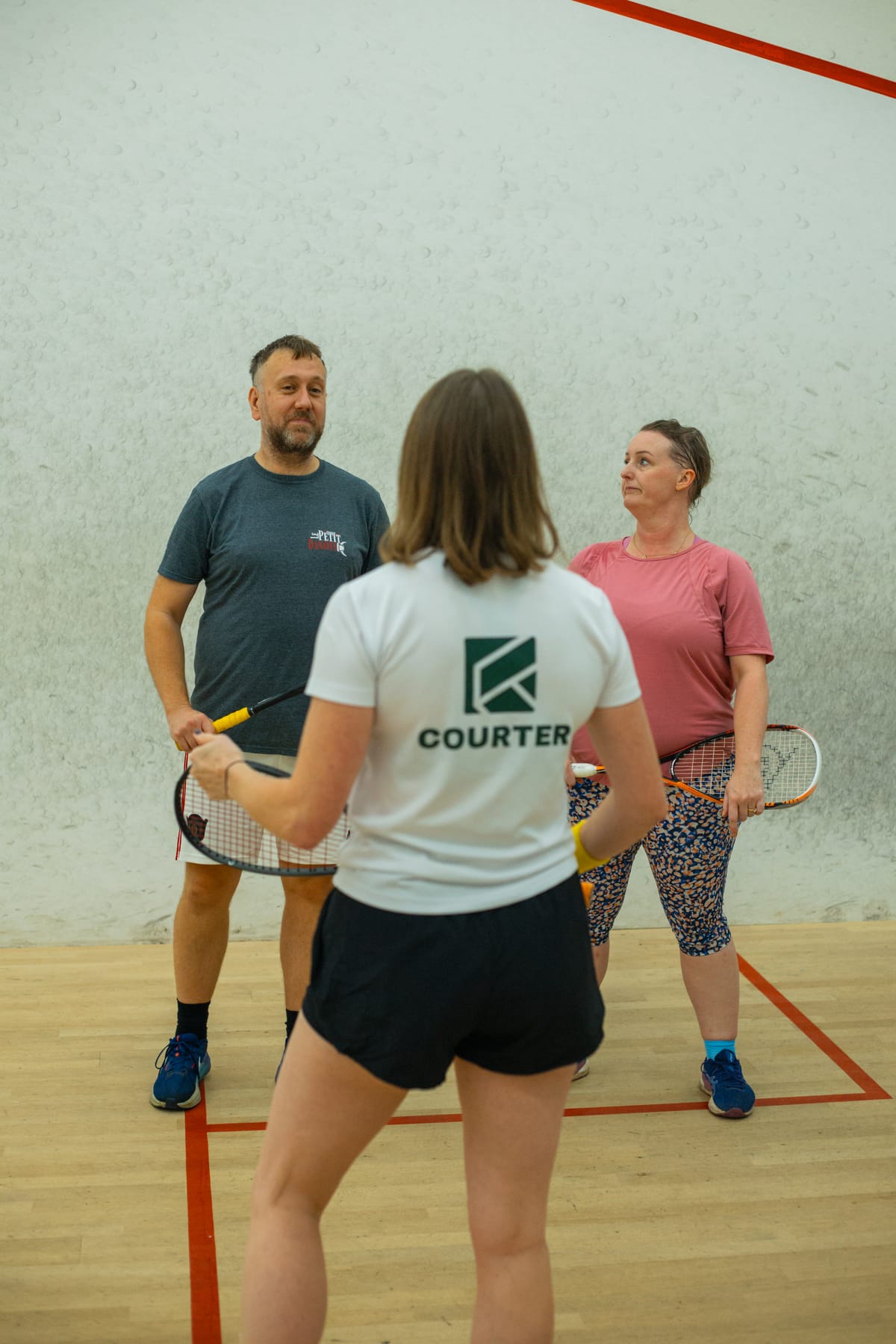 A coach in a white Courter T-shirt talking a couple through their session on court