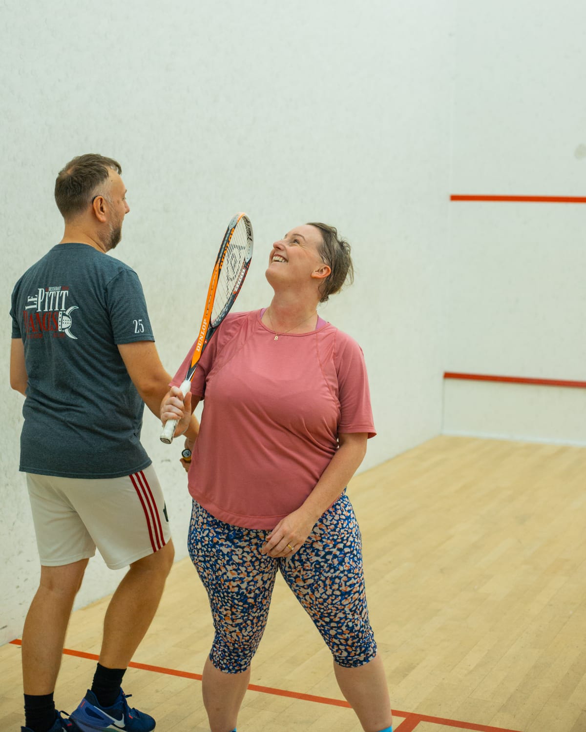 A couple laughing together on a squash court, holding their rackets